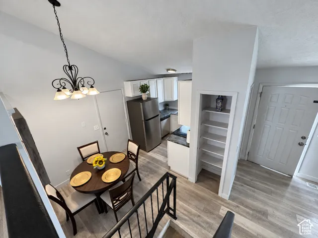 Vaulted ceiling, open kitchen layout, built-in shelving, wood-finish flooring, and a decorative chandelier