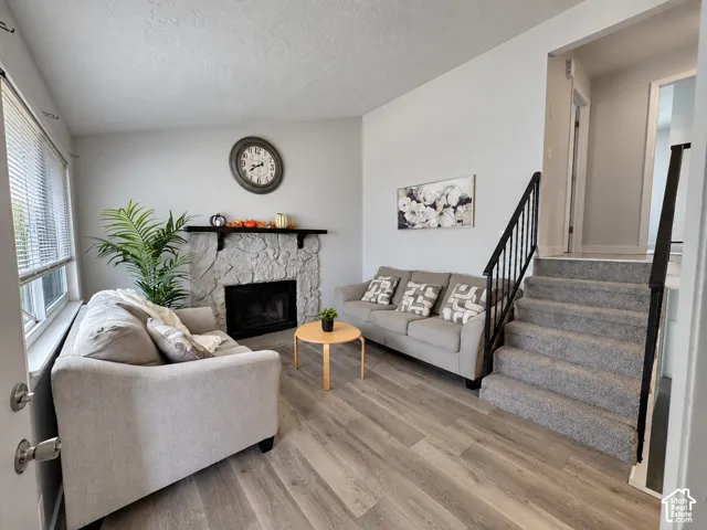 Living area featuring wood-finish flooring, a stone-faced fireplace with a black mantel, an integrated fireplace insert, and a staircase with a black metal railing
