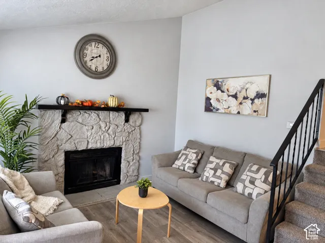 Stone-clad fireplace with a dark mantel, wood-finish flooring, and carpeted stairs with a metal railing