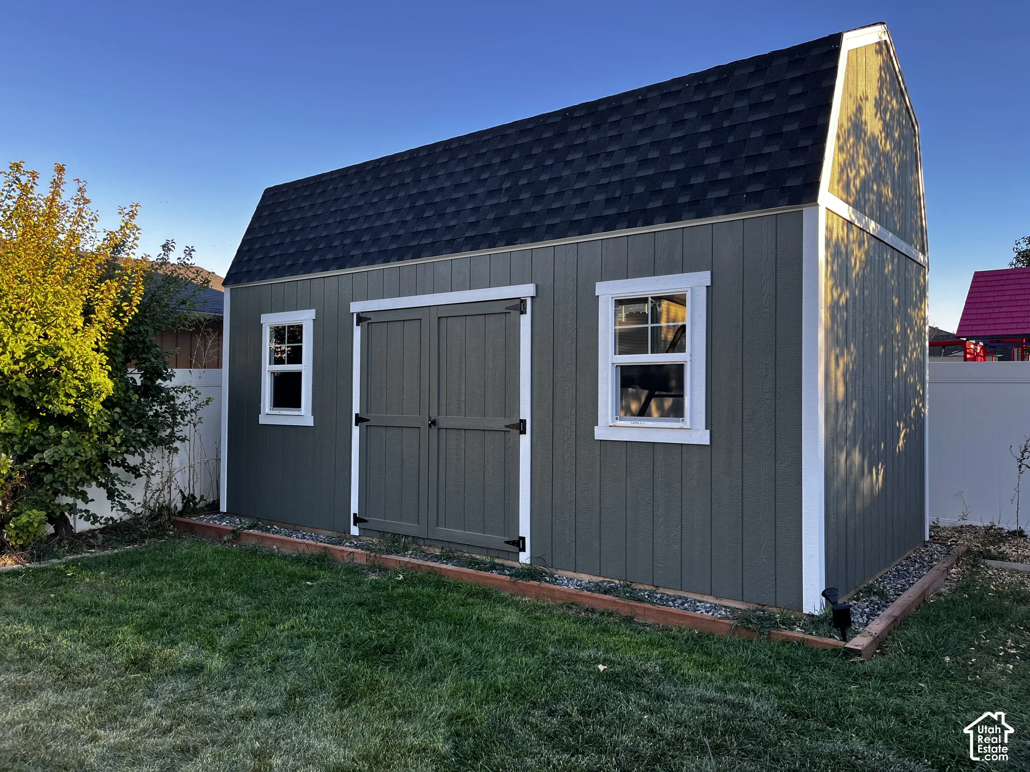 Barn-style shed with board and batten siding, dual windows, double entry doors, and a shingled roof