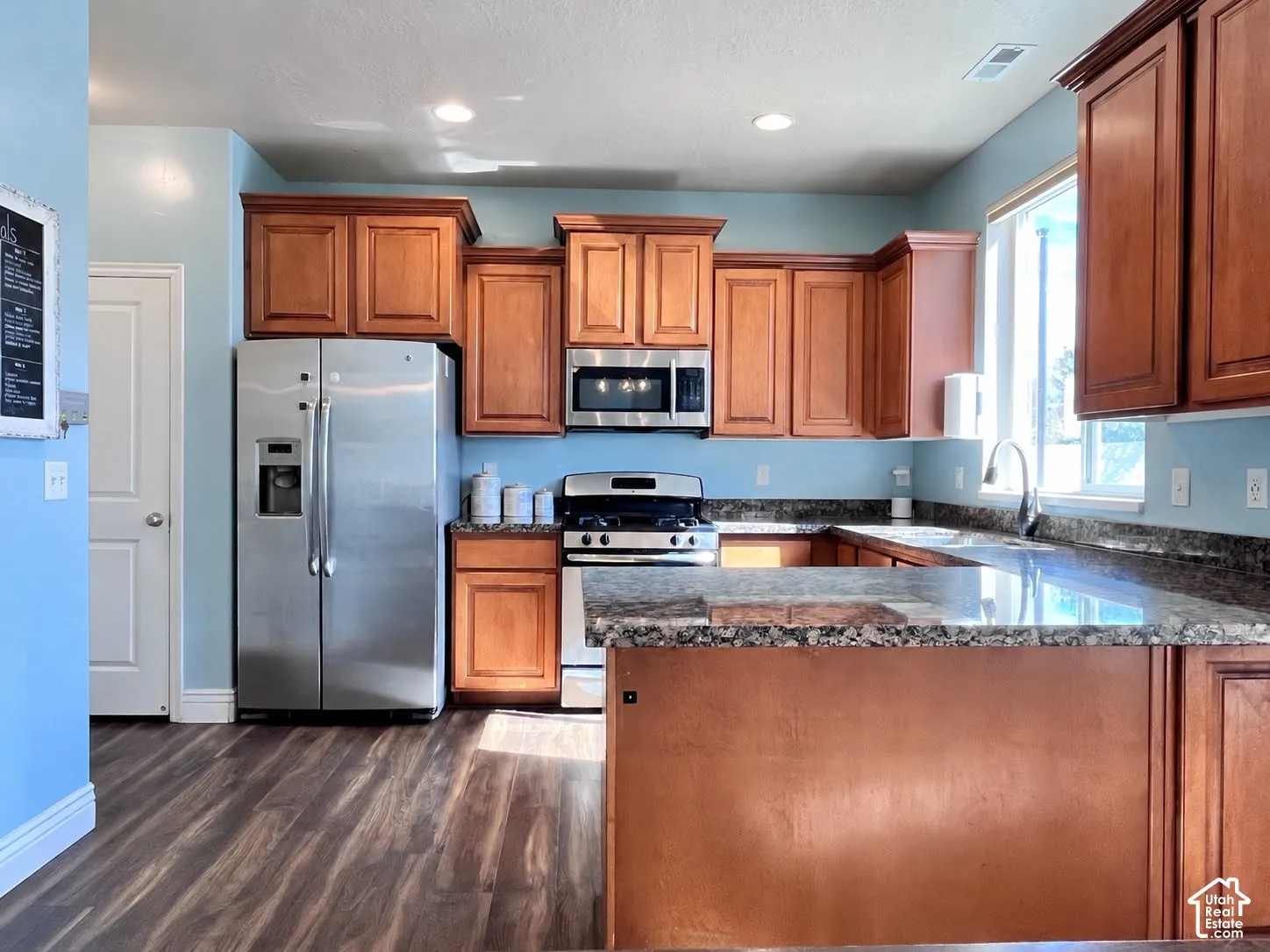 Kitchen featuring wood-finish flooring, recessed lighting, wood cabinetry, stone countertops, and stainless steel appliances