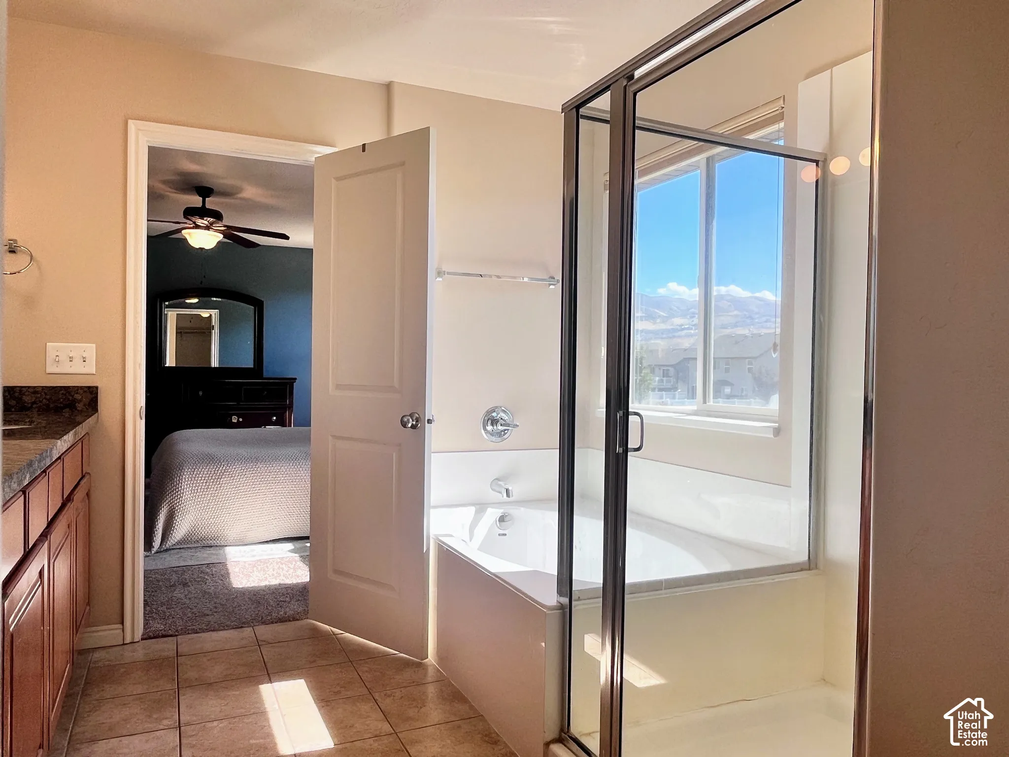 Tiled flooring, wood-finish cabinetry, built-in bathtub with glass shower enclosure, and a window with mountain scenery