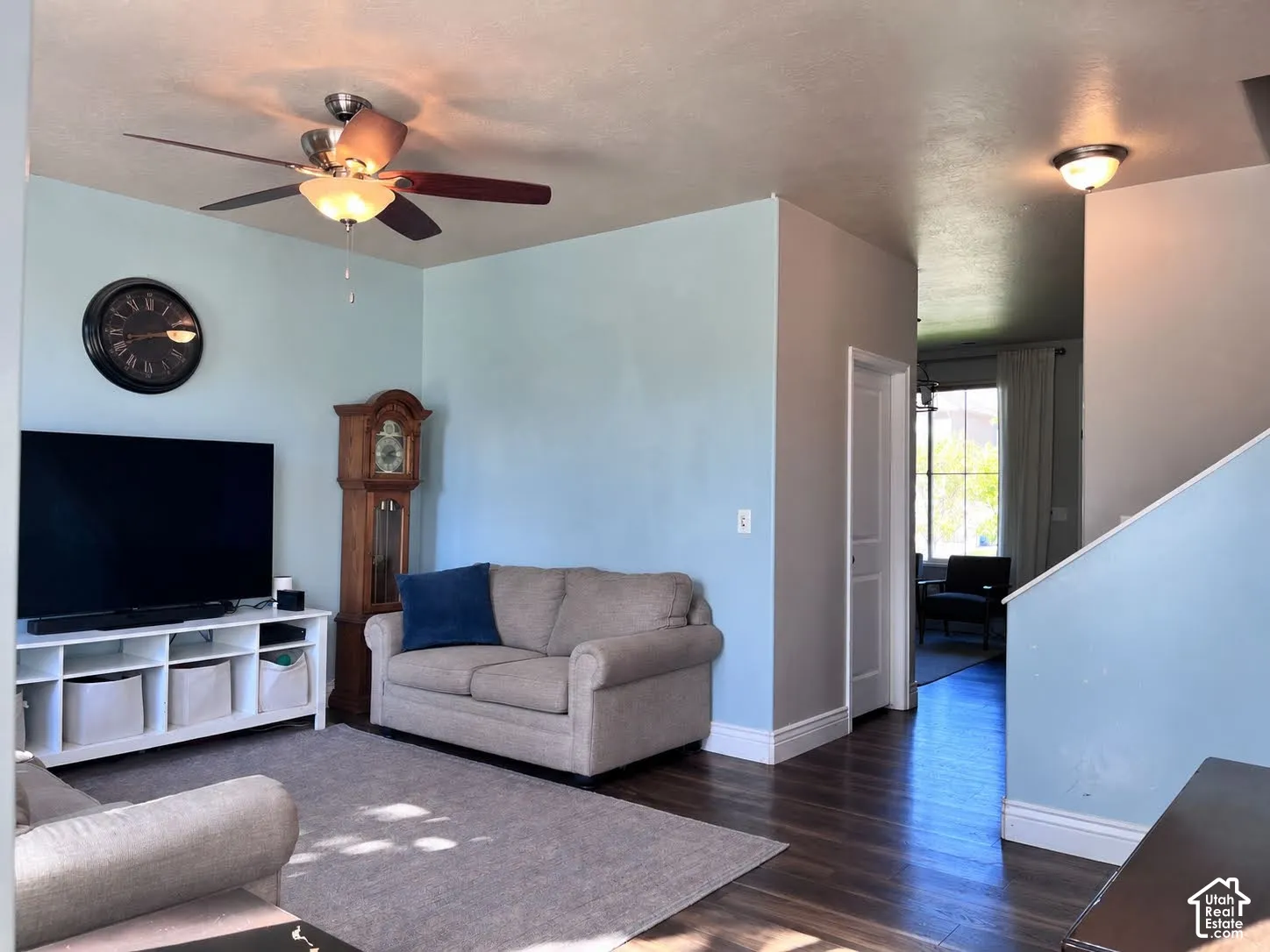 Living space featuring a ceiling fan with integrated lighting, wood-finish flooring, and white trim
