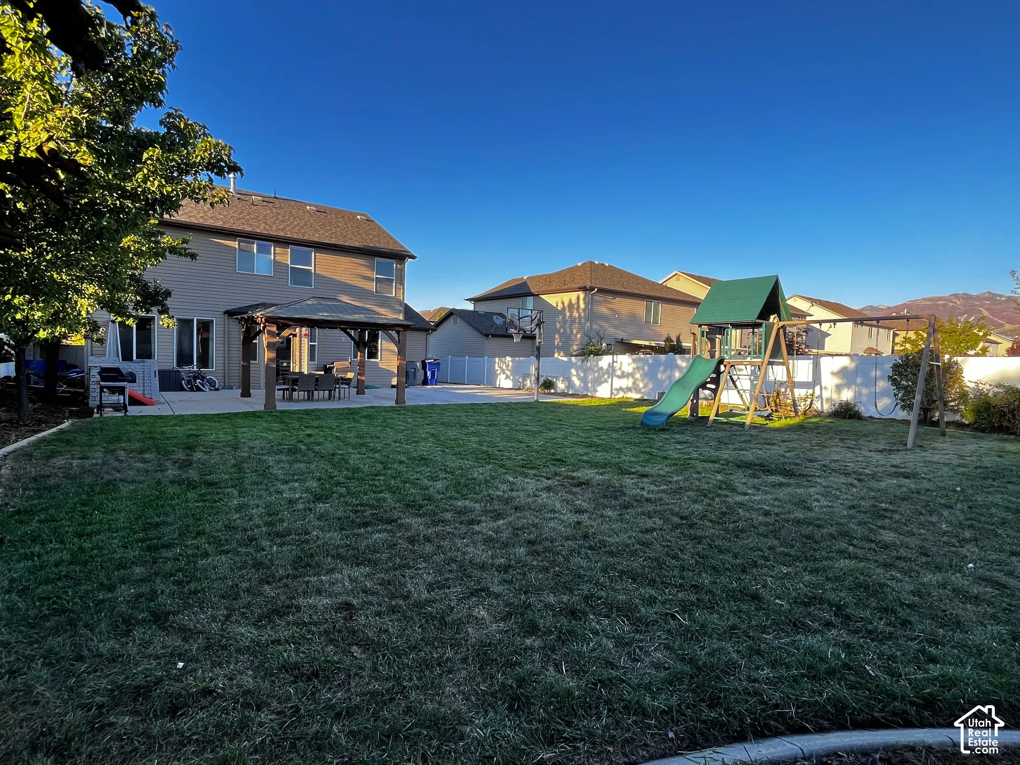 Expansive lawn area with a concrete patio, a gazebo, and a white fence