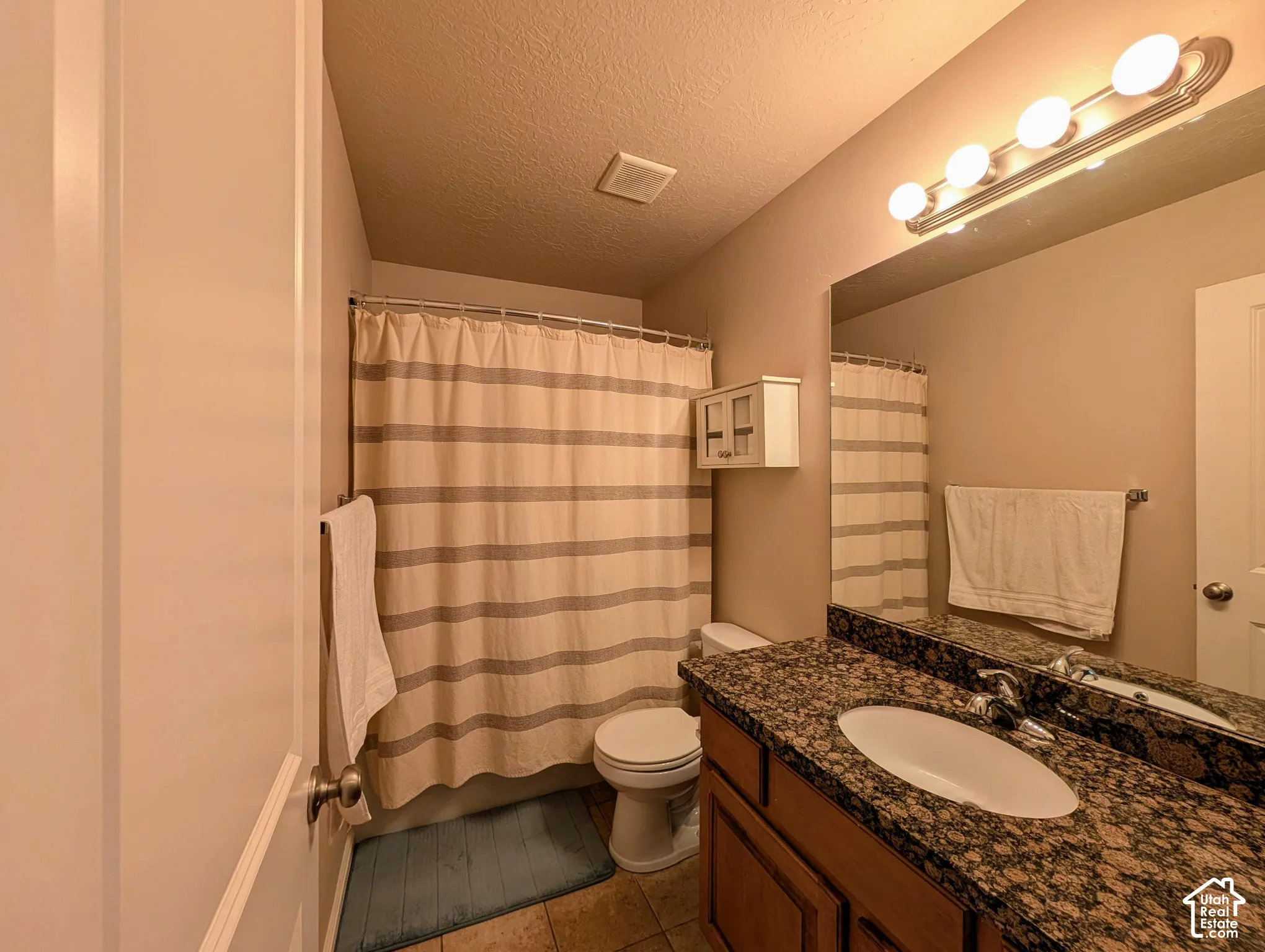 Bathroom featuring a granite-finish countertop, undermount sink, wood-finish vanity, and a shower-tub combination