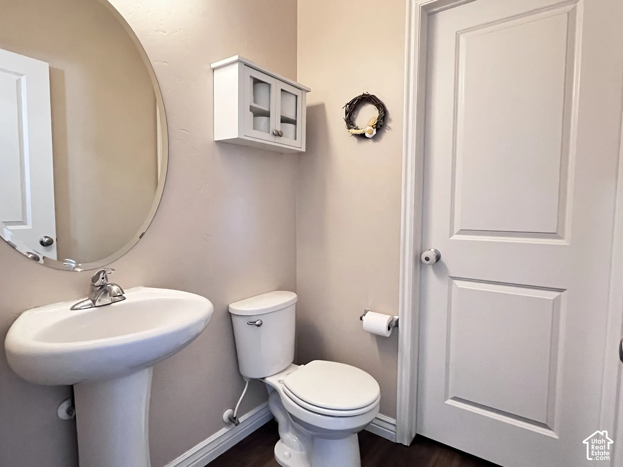 Pedestal sink, wall-mounted storage cabinet, wood-finish flooring, and a round wall mirror