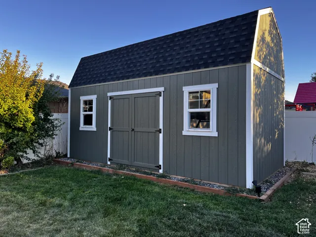 Barn-style shed with board and batten siding, dual windows, double entry doors, and a shingled roof