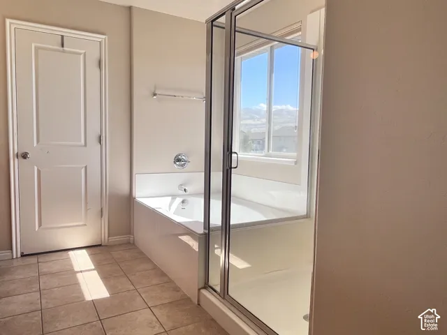 White paneled door, built-in bathtub with chrome fixtures, glass shower enclosure, large window, and tiled flooring