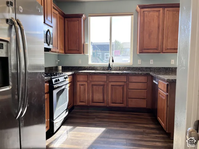 Kitchen featuring wood-finish flooring, full-height cabinetry, dark speckled countertops, and stainless steel appliances