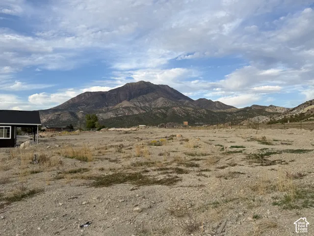 Expansive land parcel featuring a mountain backdrop and a partial structure with a dark roof and light-framed windows