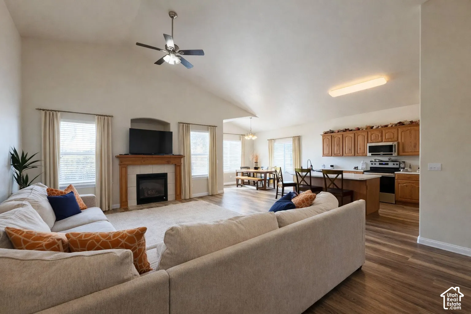 Vaulted ceilings with a ceiling fan, fireplace with a wood mantel, wood-finish flooring, and a kitchen with wood cabinetry and stainless steel appliances