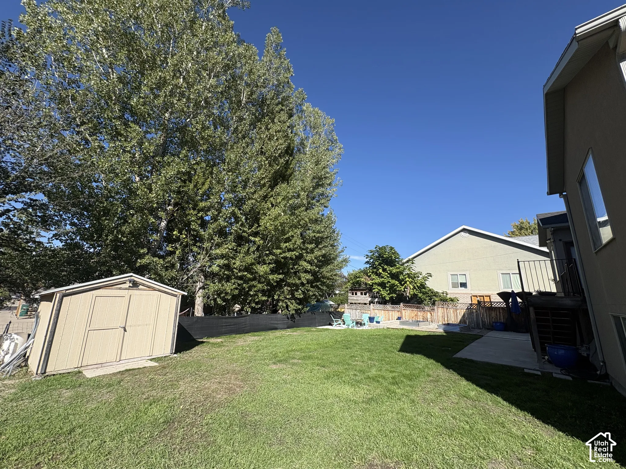 Expansive backyard featuring a manicured lawn, established trees, and a functional storage shed