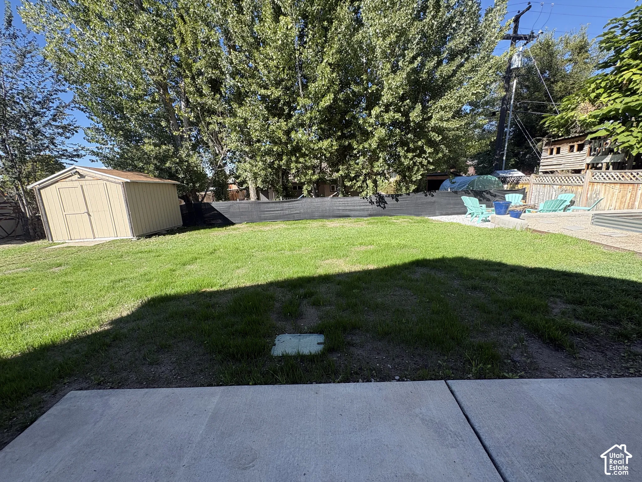 Expansive lawn area with a concrete patio, wood-paneled storage shed, and mature trees