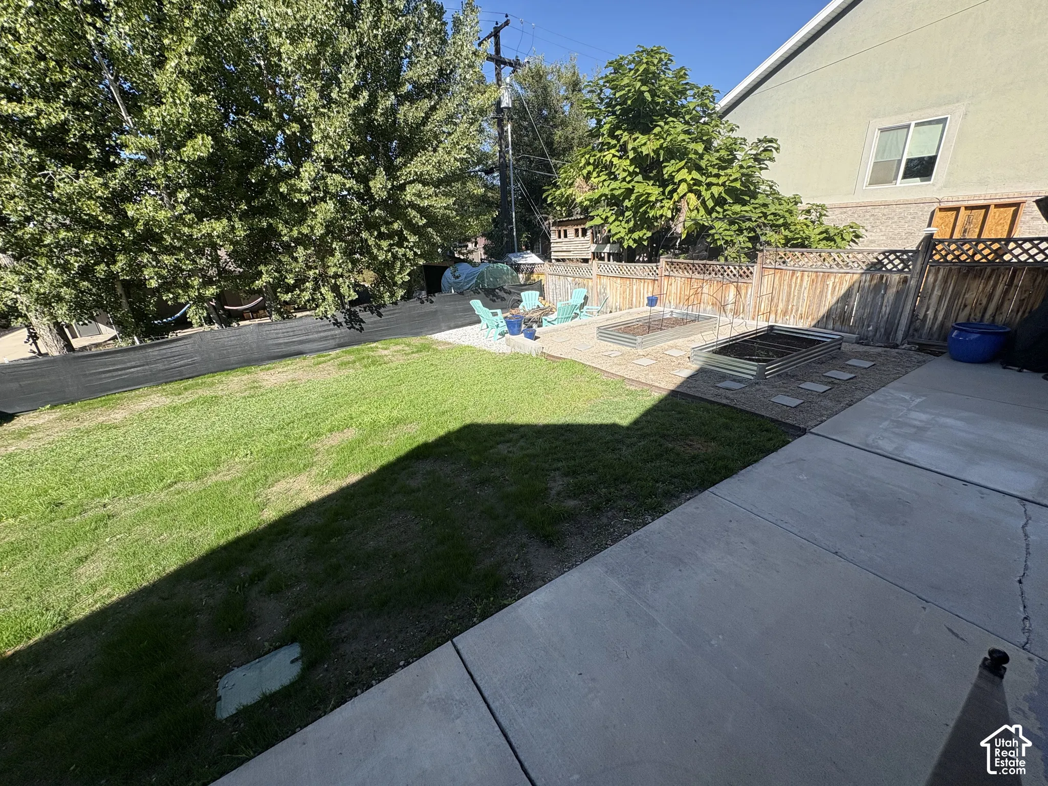 Expansive backyard featuring a concrete patio, a grass lawn, two raised garden beds, and a wood fence enclosure