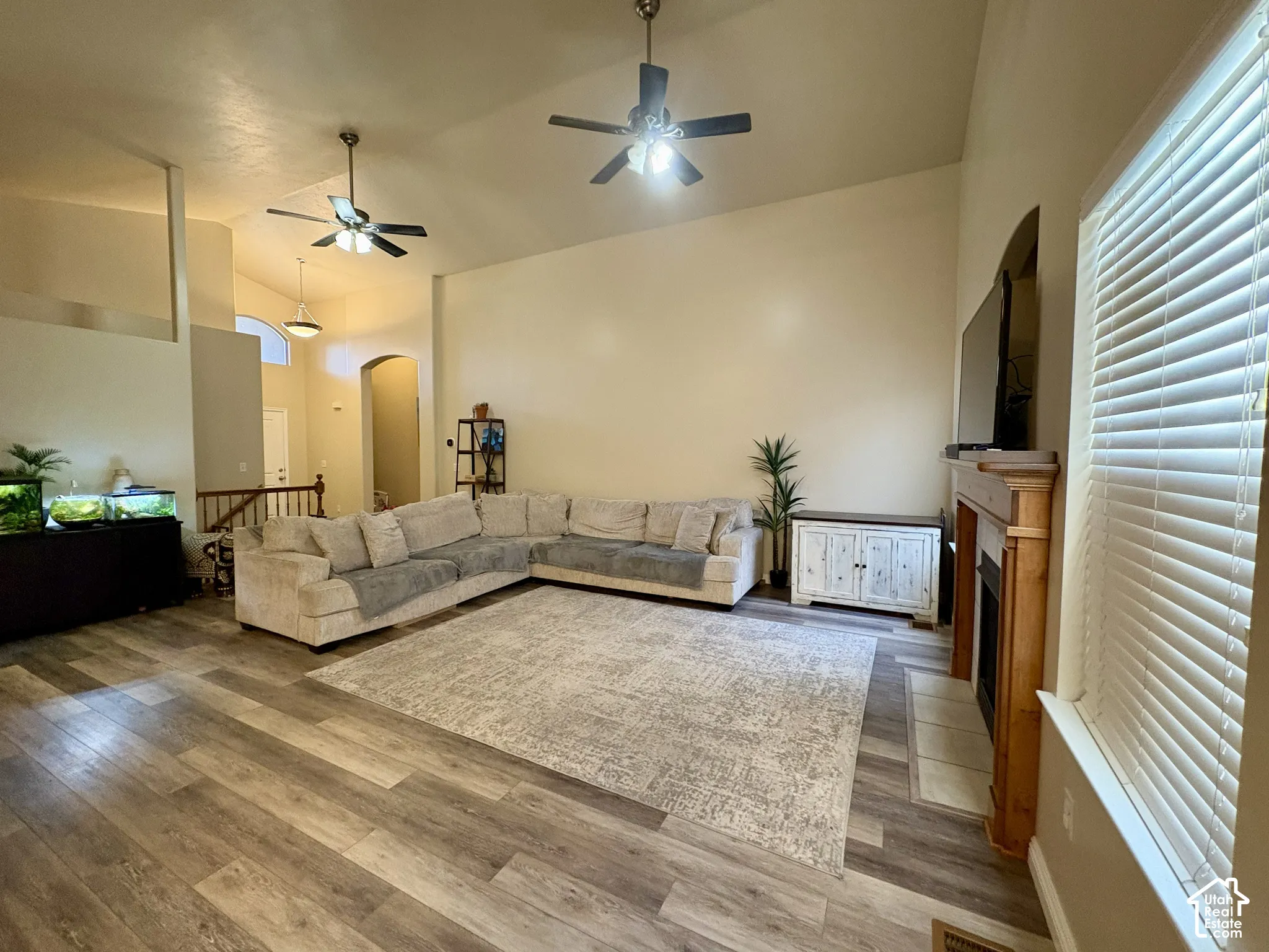 Vaulted ceilings, wood-finish flooring, two ceiling fans, a built-in fireplace with a wood mantle, and an arched entryway