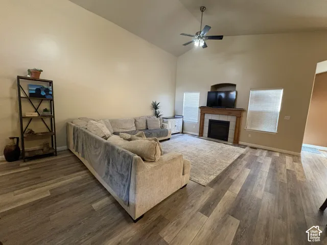 Vaulted ceilings, wood-finish flooring, built-in fireplace with tile surround and wood mantel, ceiling fan with integrated lighting, and multiple windows