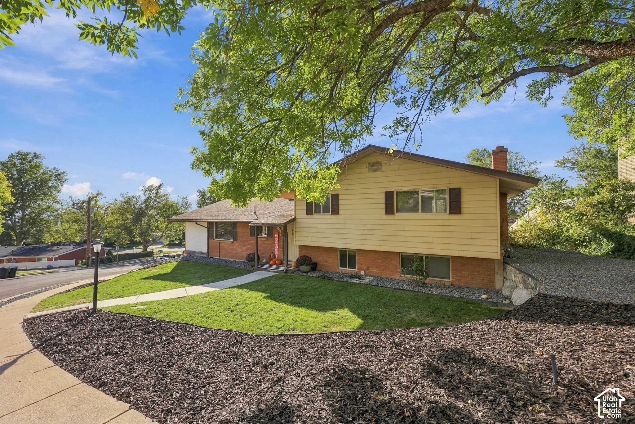 Split-level residence featuring a brick and siding exterior, front yard with green lawn, paved driveway, and mature trees