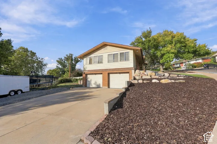 Split-level residence featuring a two-car garage with individual doors, a concrete driveway, and a front yard with bark mulch and decorative boulders