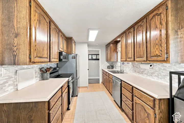 Galley kitchen featuring wood cabinetry, light countertops, mosaic tile backsplash, and stainless steel appliances