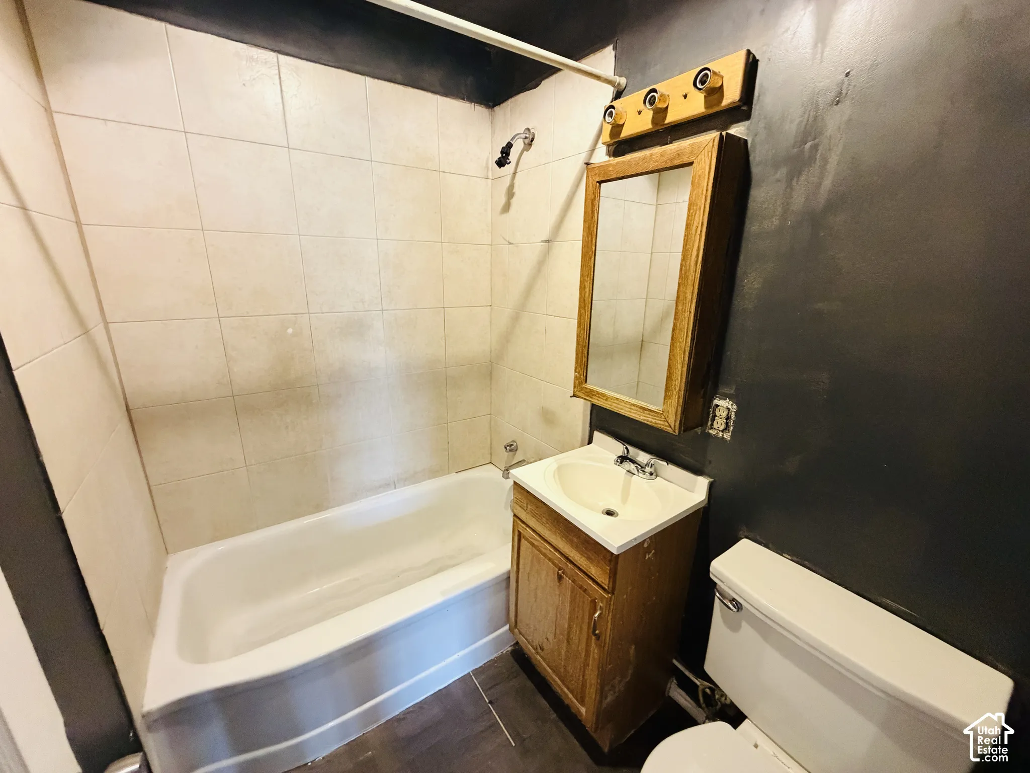 White tiled shower surround, built-in bathtub, wood-finish vanity with integrated sink, wood-framed medicine cabinet, and toilet
