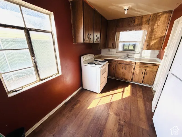 Wood-finish flooring with an integrated kitchen featuring wood cabinetry, white tile backsplash, and a white sink
