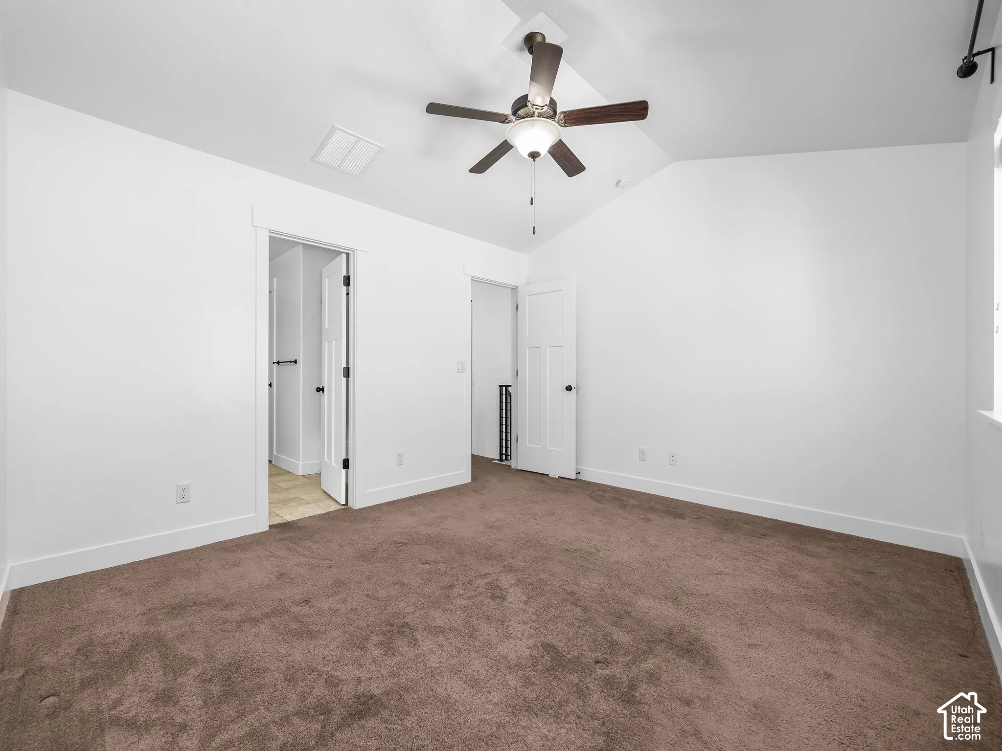 Vaulted ceiling with a ceiling fan, white paneled doors, and brown carpeting