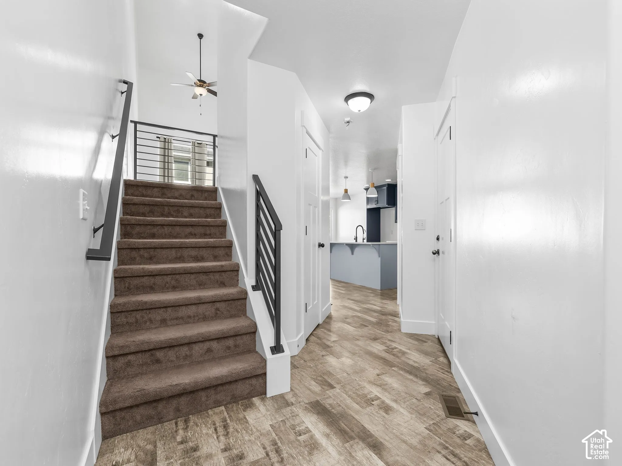 Carpeted staircase with black metal railing, wood-finish flooring, and white walls