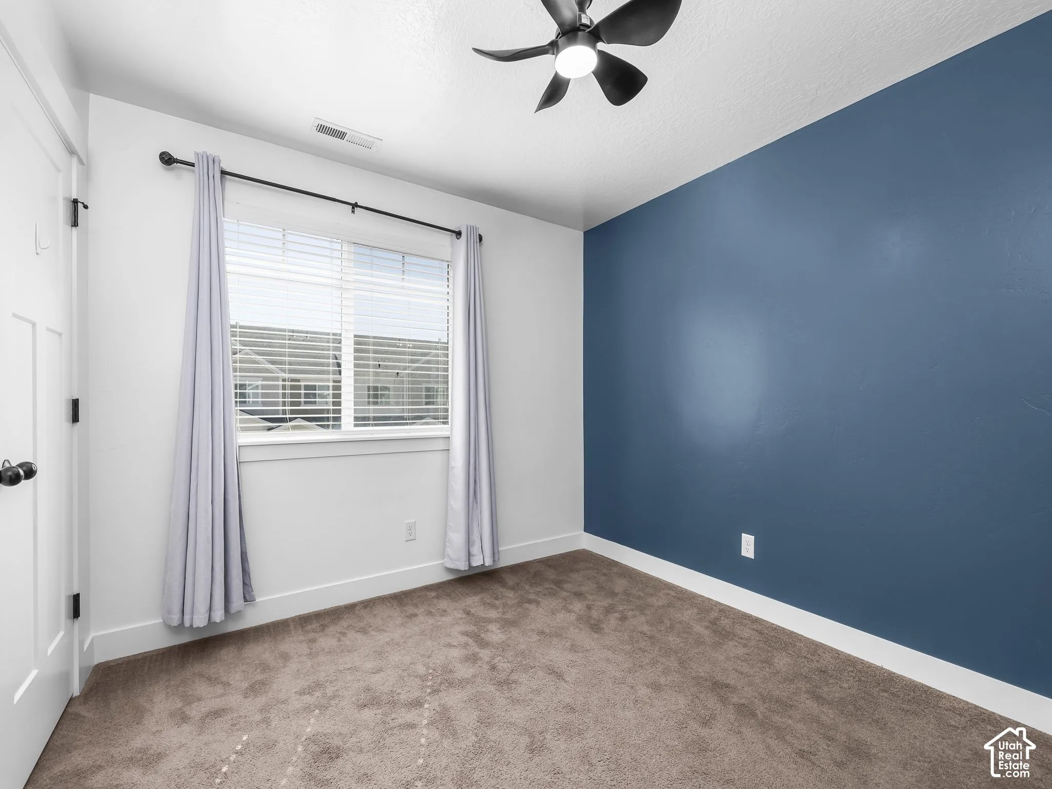 Carpeted room featuring a ceiling fan with integrated lighting, a window with blinds, and a paneled interior door