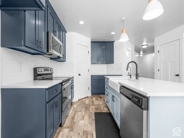 Kitchen featuring blue cabinetry, a white tile backsplash, light-toned countertops, wood-finish flooring, and pendant lighting