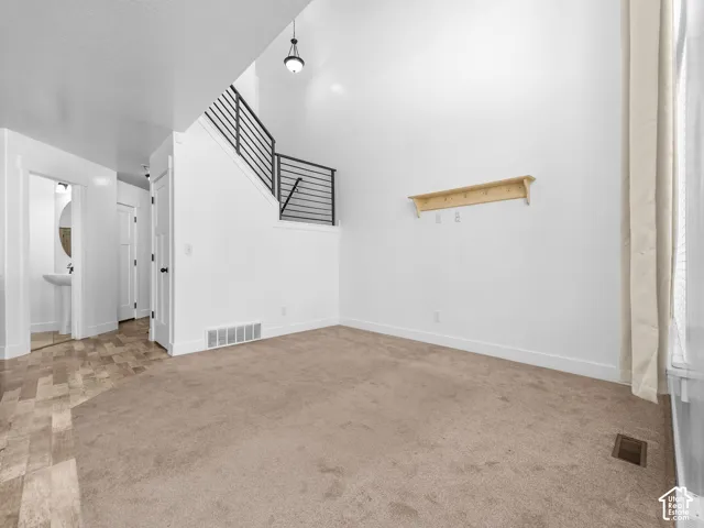 Vaulted ceiling with a pendant light fixture, carpeted flooring, and a contemporary stair railing