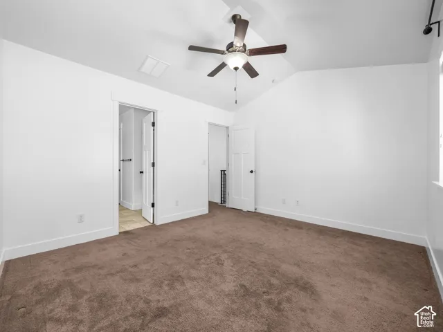 Vaulted ceiling with a ceiling fan, white paneled doors, and brown carpeting