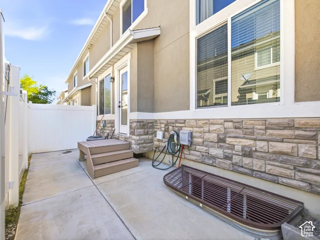 Exterior featuring a stucco facade, stone veneer detailing, a white vinyl privacy fence, a concrete patio, and a multi-pane glass door with a transom window