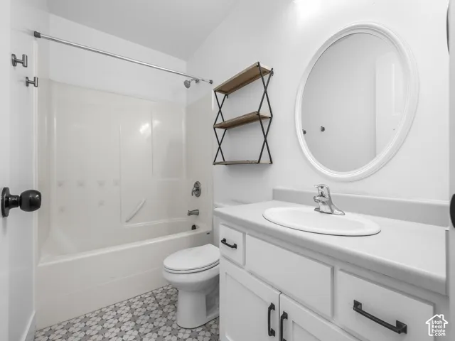 Bathroom featuring a white vanity with black pulls, oval mirror, white shower/tub combination, and patterned floor tile