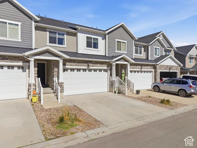 Two-story townhouse with a single-car garage, stone and siding exterior, covered porch entry, concrete driveway, and a shingled roof