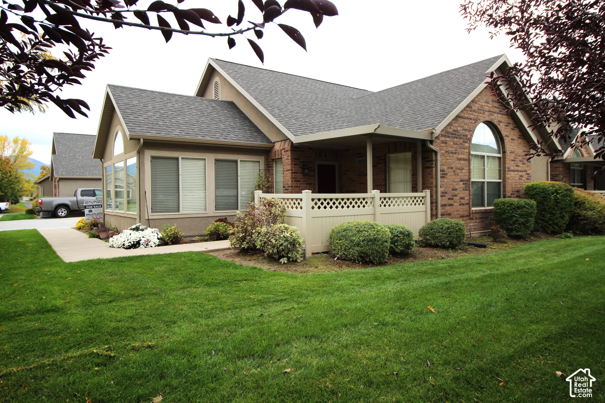 Exterior featuring a brick and stucco facade, an arched window, a covered porch with decorative latticework railing, and a concrete walkway