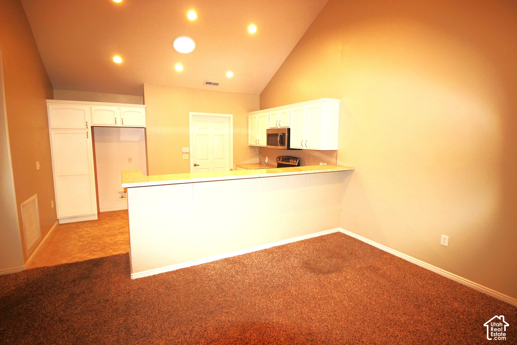 Vaulted ceilings featuring recessed lighting, white cabinetry, built-in microwave, and peninsula counter