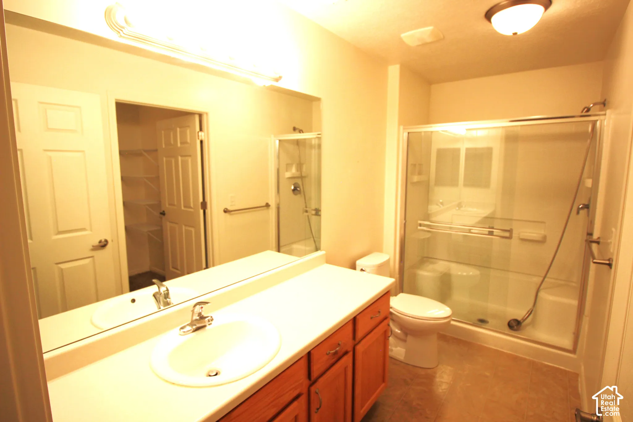 Master Bathroom featuring a vanity with integrated sink, wood-finish cabinetry, full-width wall mirror, and a glass-enclosed shower with a built-in seat