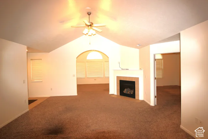 Vaulted ceiling with an integrated light-and-fan fixture, gas fireplace with a mantle and tile surround, and an arched architectural opening