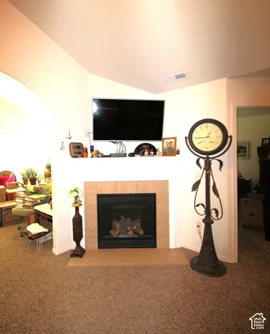 Corner fireplace with a tile surround and hearth, featuring a white mantel, beige carpet, and vaulted ceiling
