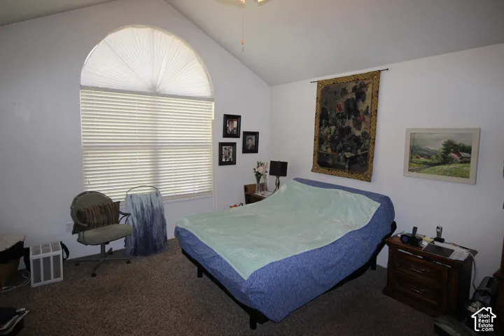 Vaulted ceiling with a ceiling fan, arched window with pleated shades, and carpeted flooring