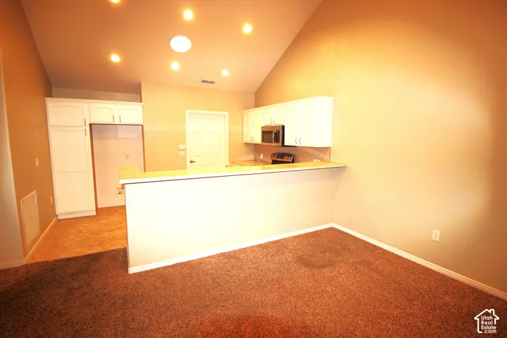 Vaulted ceilings featuring recessed lighting, white cabinetry, built-in microwave, and peninsula counter