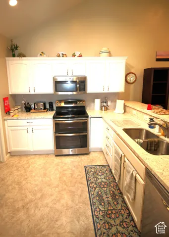 Kitchen featuring white cabinetry, light-toned countertops, stainless steel appliances, a double basin sink, and a vaulted ceiling