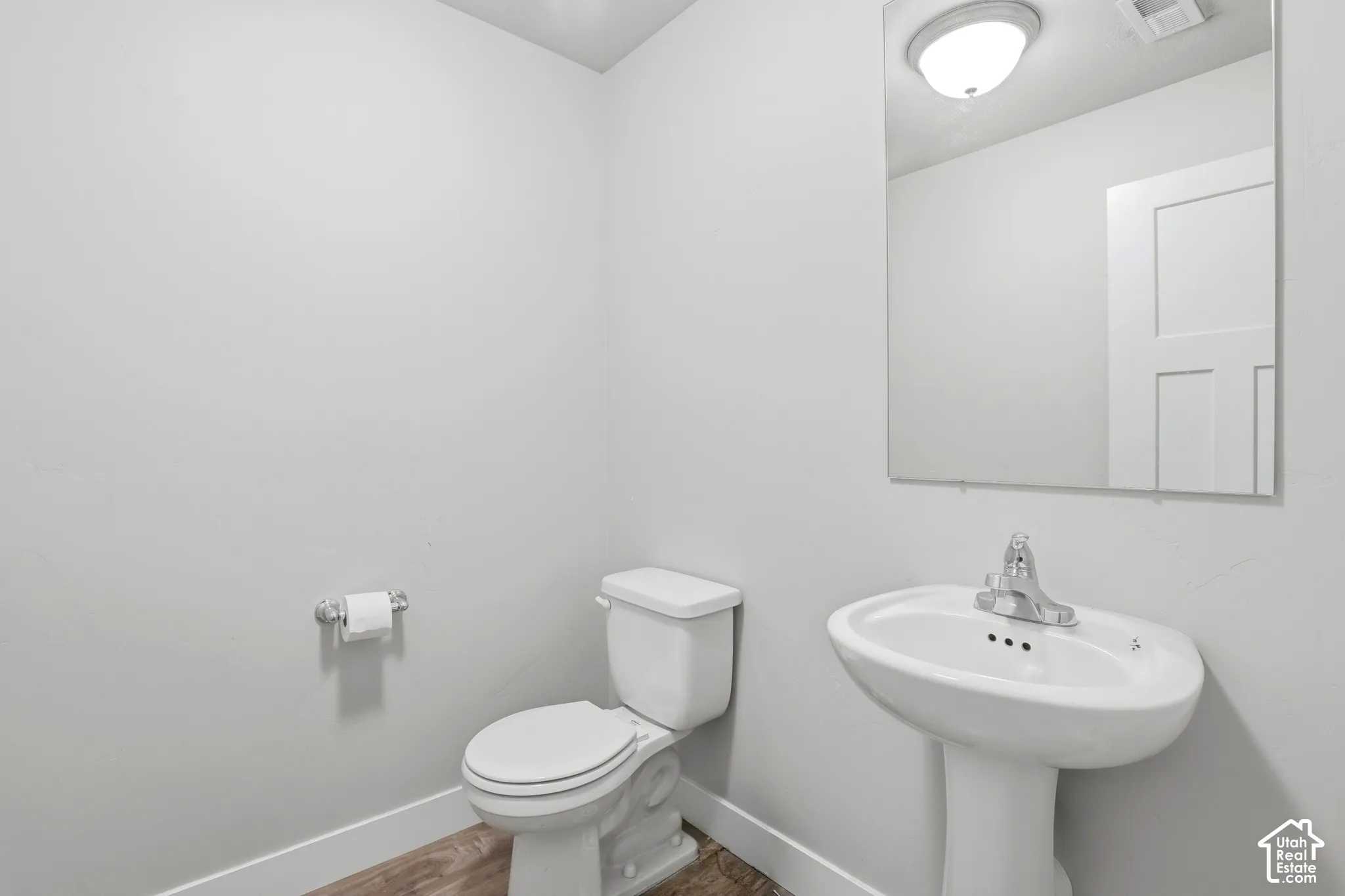 Pedestal sink with chrome fixtures, an overhead light fixture, and a rectangular wall-mounted mirror