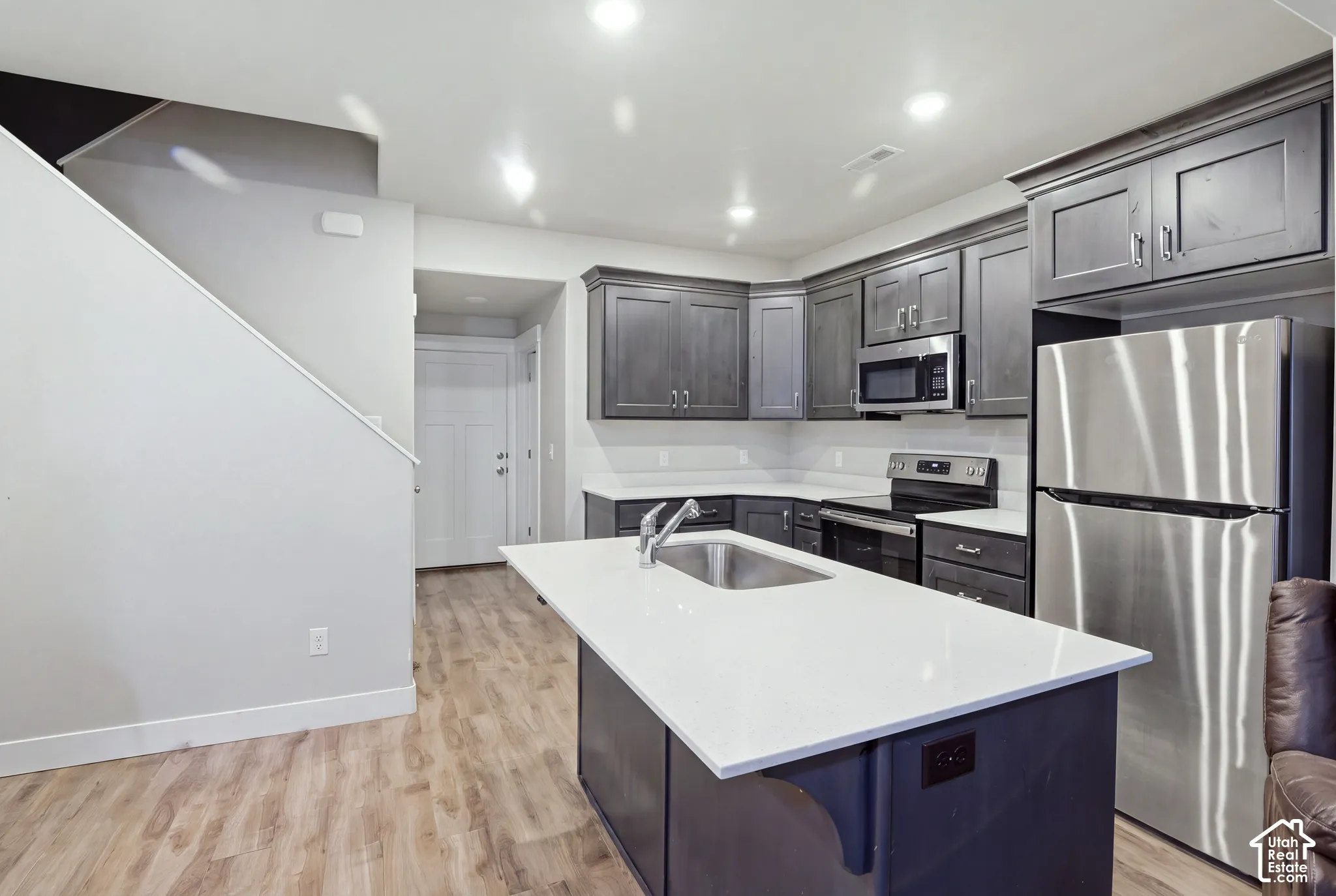 Kitchen featuring dark wood cabinetry, stainless steel appliances, white countertops, and a center island with an undermount sink
