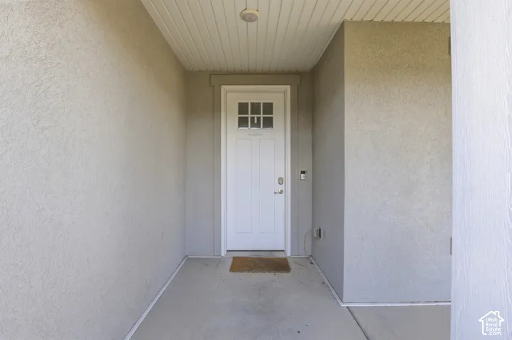 Recessed entry with stucco walls, a paneled white door with upper window panes, and a beadboard ceiling