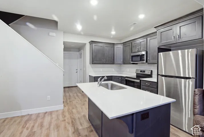 Kitchen featuring dark wood cabinetry, stainless steel appliances, white countertops, and a center island with an undermount sink