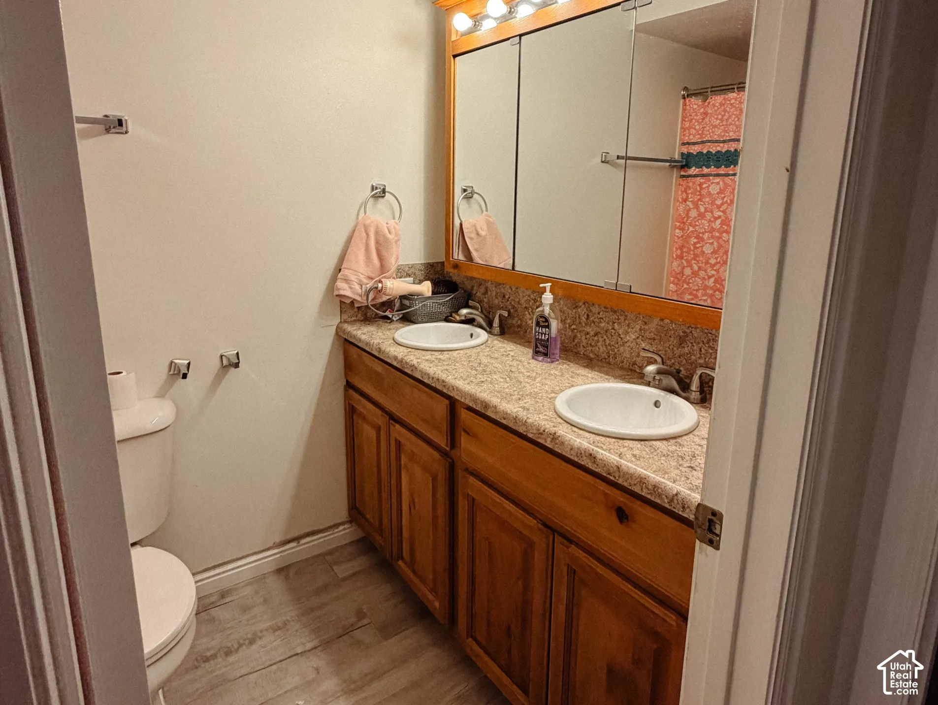 Dual vanity with integrated sinks, wood-finish cabinetry, a large mirror, and light wood-finish flooring