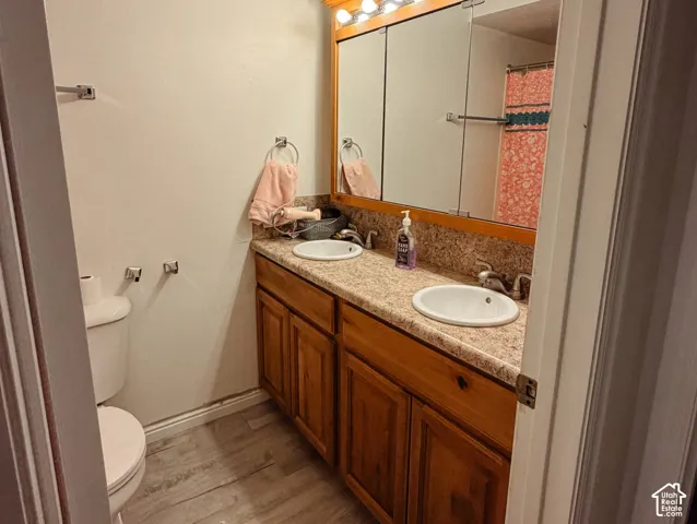 Dual vanity with integrated sinks, wood-finish cabinetry, a large mirror, and light wood-finish flooring