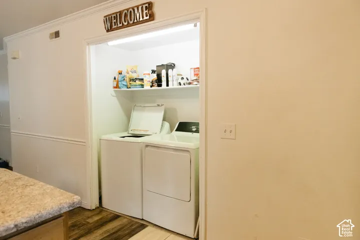 Built-in laundry nook featuring overhead shelving, wood-finish flooring, and crown molding