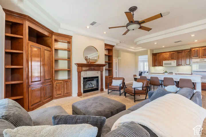 Built-in cabinetry, fireplace with stone surround, recessed lighting, ceiling fan, and tray ceiling